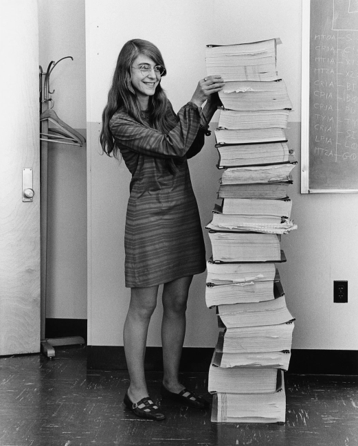 Margaret Hamilton at the MIT Instrumentation Lab, beside a stack of AGC source code as tall as she is